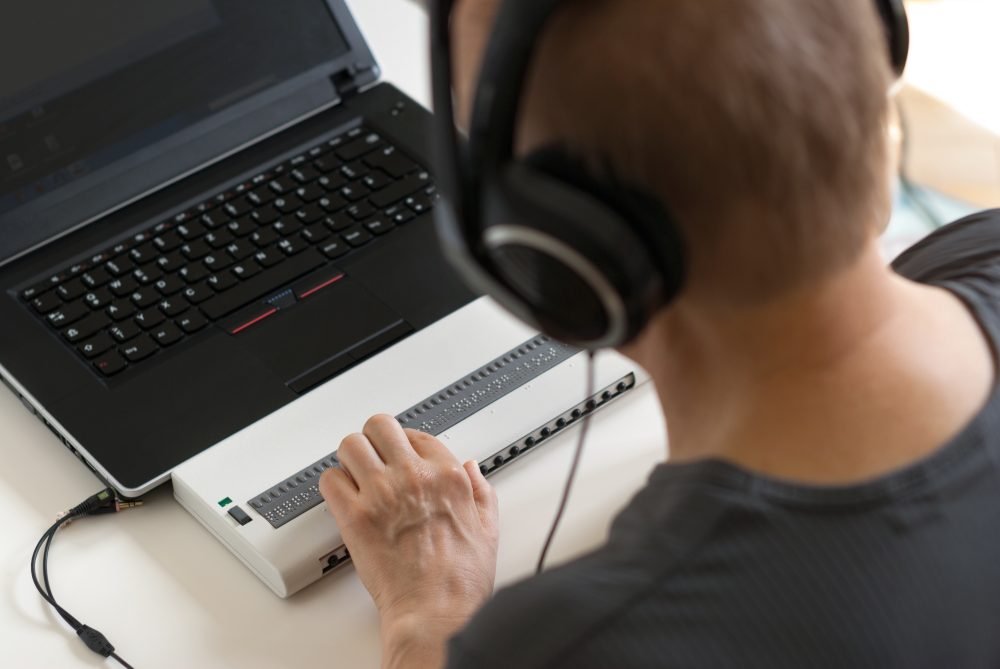 A person who is blind accessing information on a computer with a braille display and screen reader.