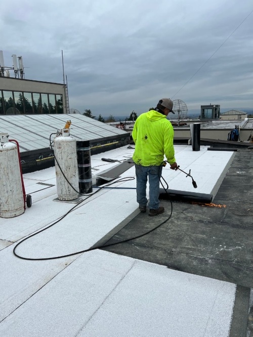 Worker using a torch to apply a cap on the College Center roof