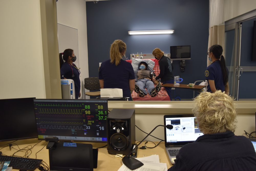 Students in the patient room, surround the patient (smart mannequin) which is control from another room by the instructor