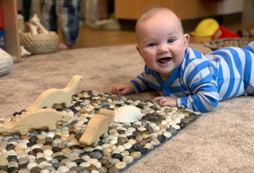 Baby playing on the ground with dinosaurs and smiling