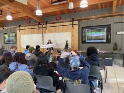Denise Berkshire holds a sign in front of a crowd inside the Forest Center's Community Hall that reads 'anadromous', meaning species of fish that migrates between salt and fresh water. 