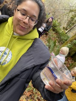 Cassidy Campbell, a PCC student, contemplates her cup of little salmon fry while standing in the woods around Jones Creek. 