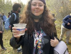 PCC Multimedia student Reo Moore stands with her small cup of water, containing 2 Swim-Up fry salmon, ready to be released into Jones Creek. 