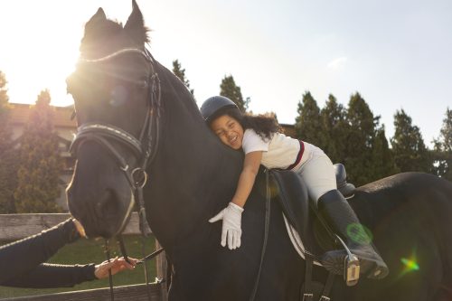 Child in saddle on horse giving it a hug.