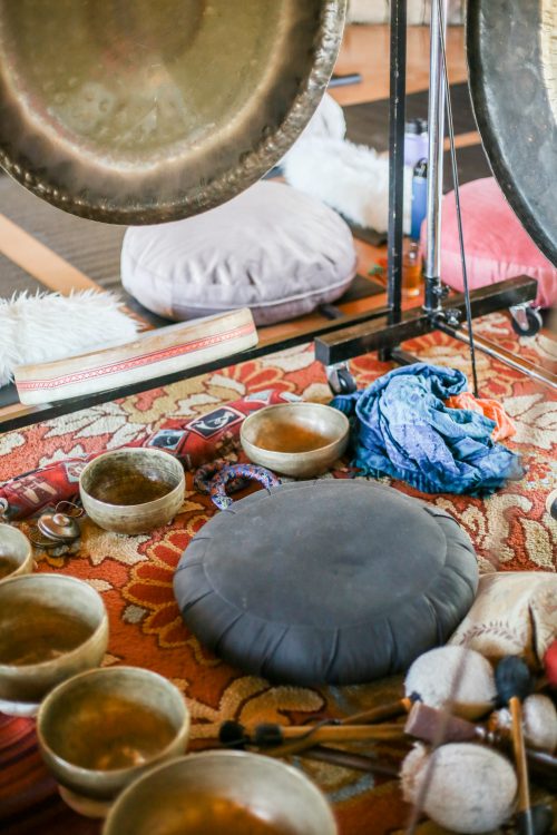 Singing bowls and gongs surrounding a cushion on the ground.