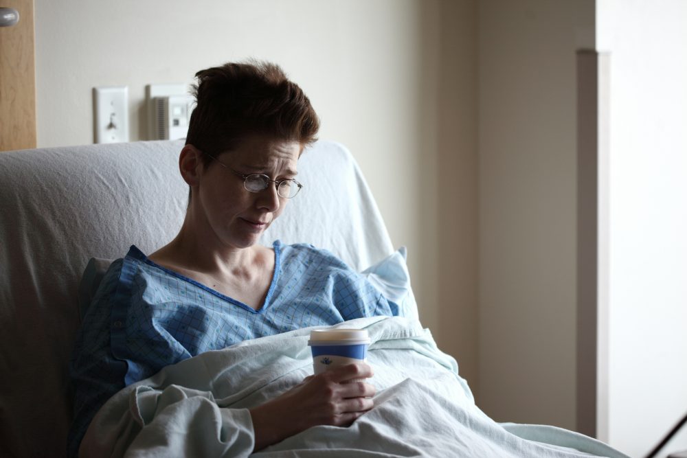 A woman looking sad sitting in a hospital bed.