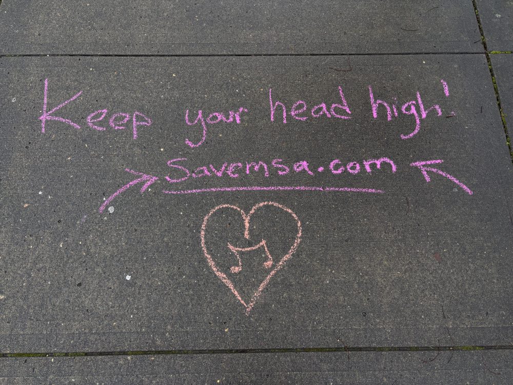 Chalk art on sidewalk that reads: "Keep your head high! Savemsa.com." A heart with a music note is drawn below the writing.