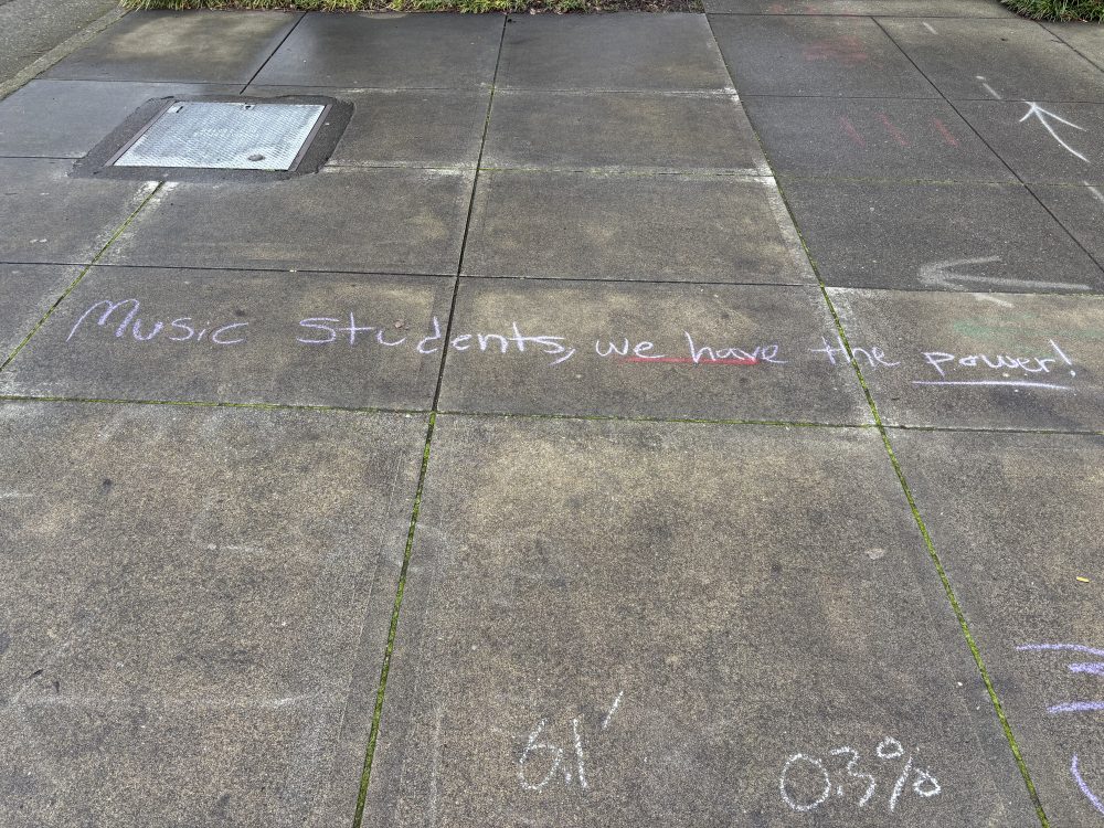 Chalk art on sidewalk that reads: "Music students, we have the power!"
