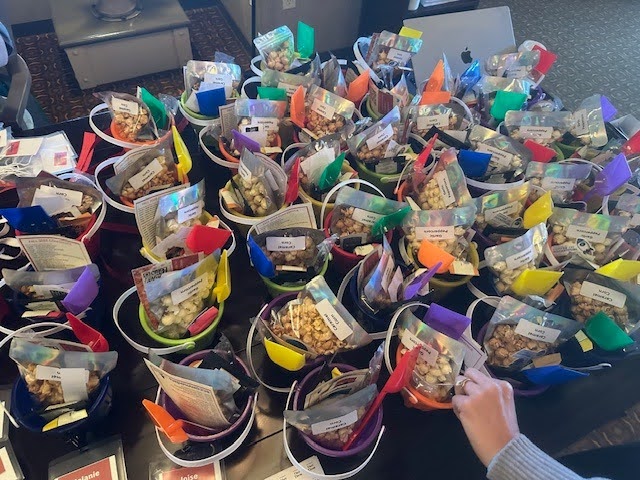 Dozens of small plastic buckets on a table with bags of popcorn and tiny plastic shovels in them.