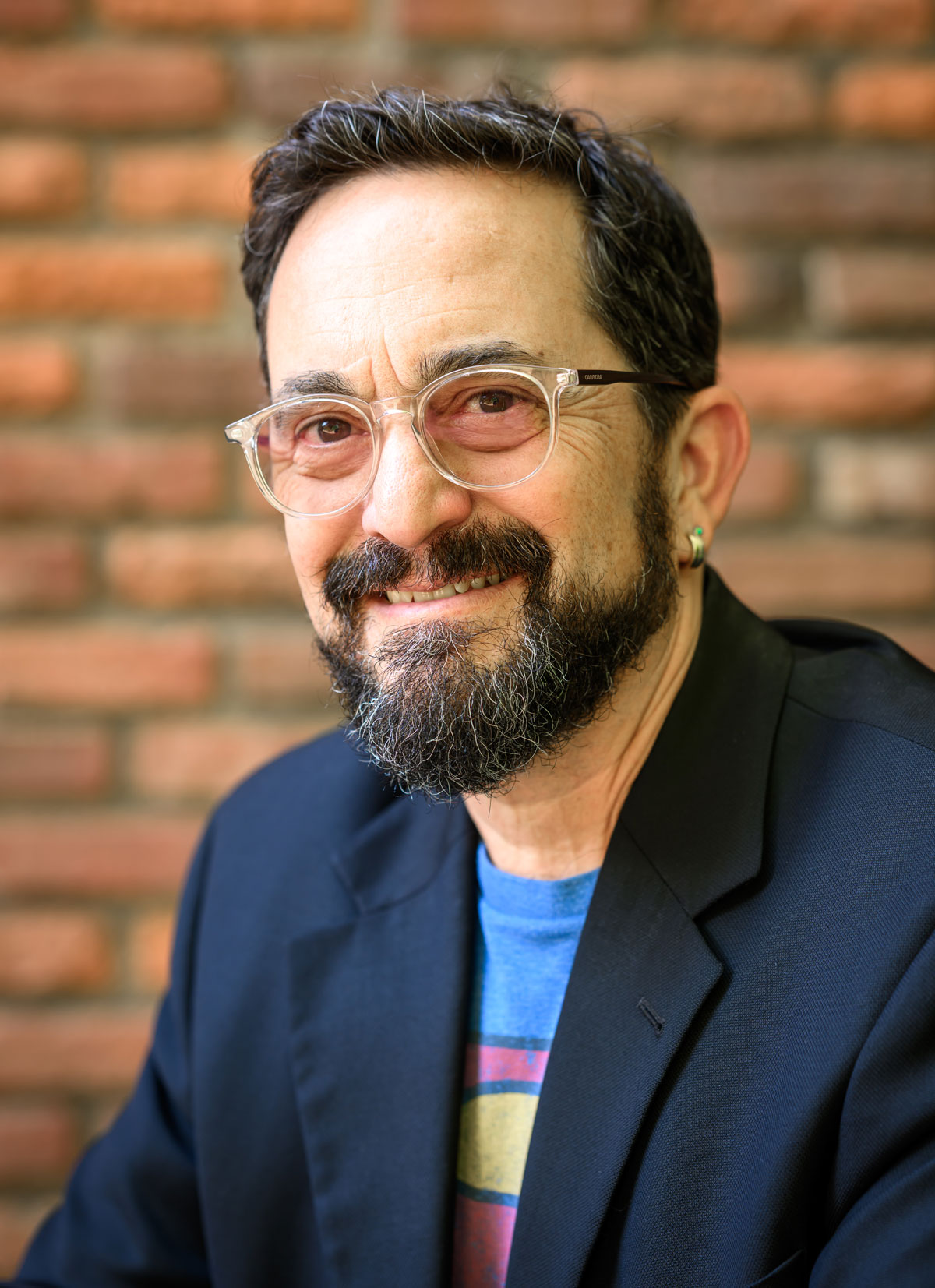 Photo of the author, Caleb Dardick, who has light skin tone, dark short hair and a beard, and light red-tinted glasses. He is wearing a blazer over a Superman logo shirt, and smiling.