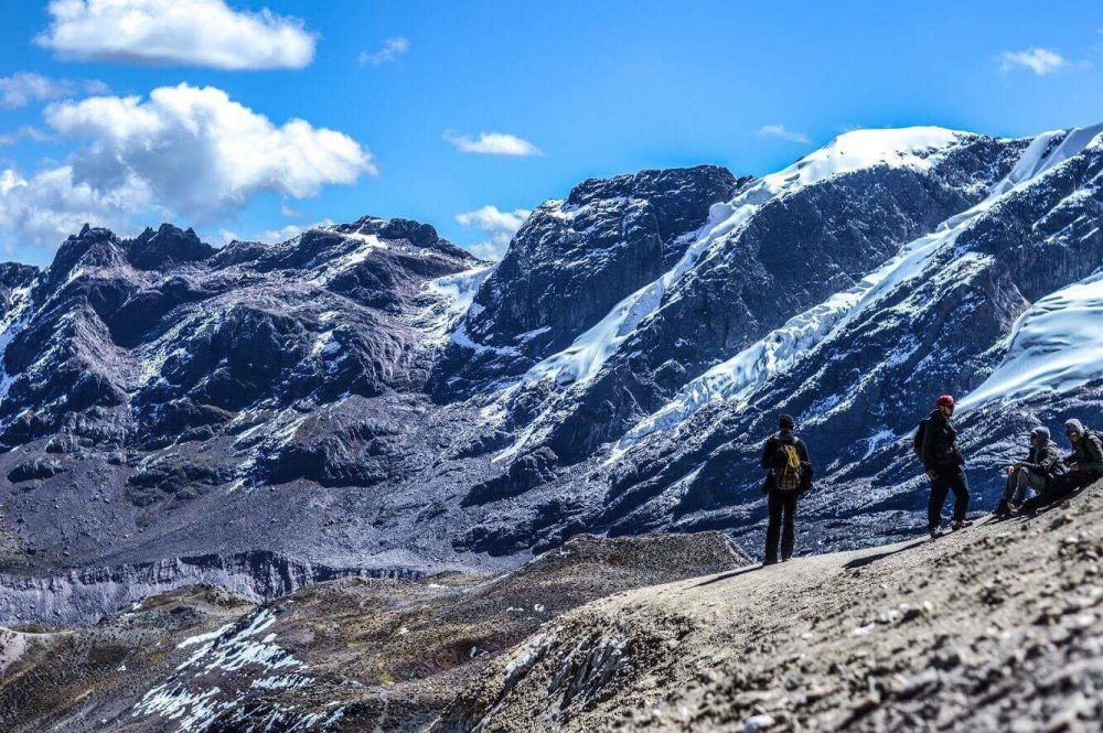 Photo of rocky mountains with some snow, hikers standing in the foreground.