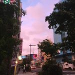 A photo of a city street at sunrise, with a light pink and blue sky.