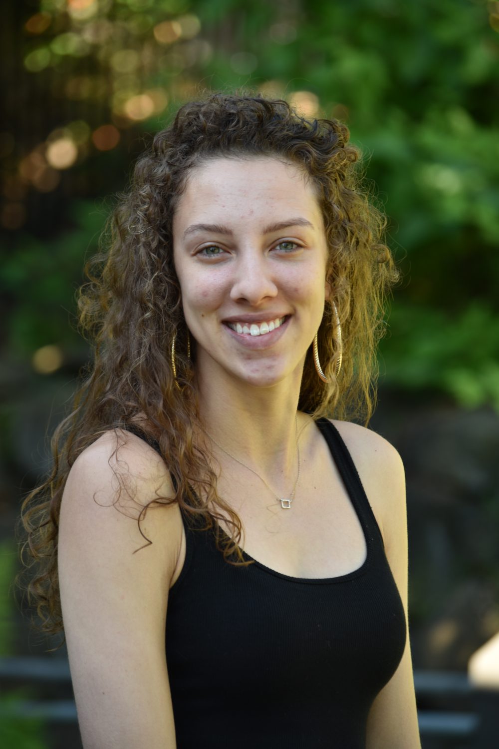 Emory Neer, 2018-19 EAO Peer Mentor, portrait photo of female with curly hair, wearing a black tank top, large golden earrings, and a necklace.