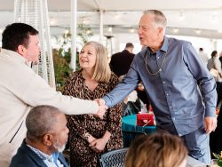 Two men shake hands next to a smiling woman