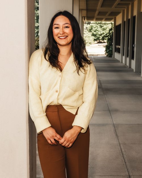 Person standing and leaning against a concrete pillar in a breezeway.