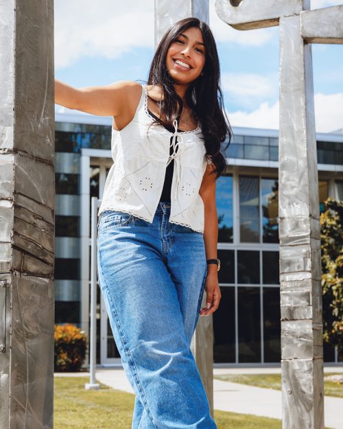 Student standing on metal sculpture with right hand holding on to metal upright and right leg kicked out.