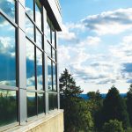 Blue sky with clouds and treetops are reflected in large windows on the side of a building on the PCC Sylvania campus