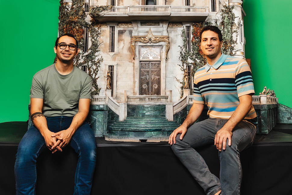Two people sitting on a stage with a large model of Pittock Mansion that will be in the film Wildwood.