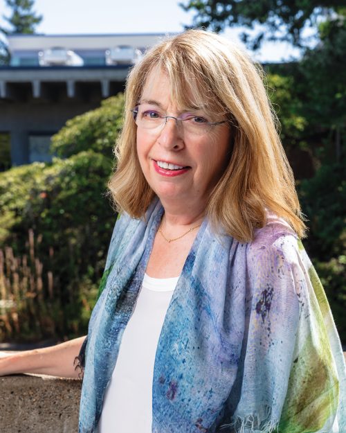 Woman wearing glasses turned sideways and looking directly at the camera smiling.