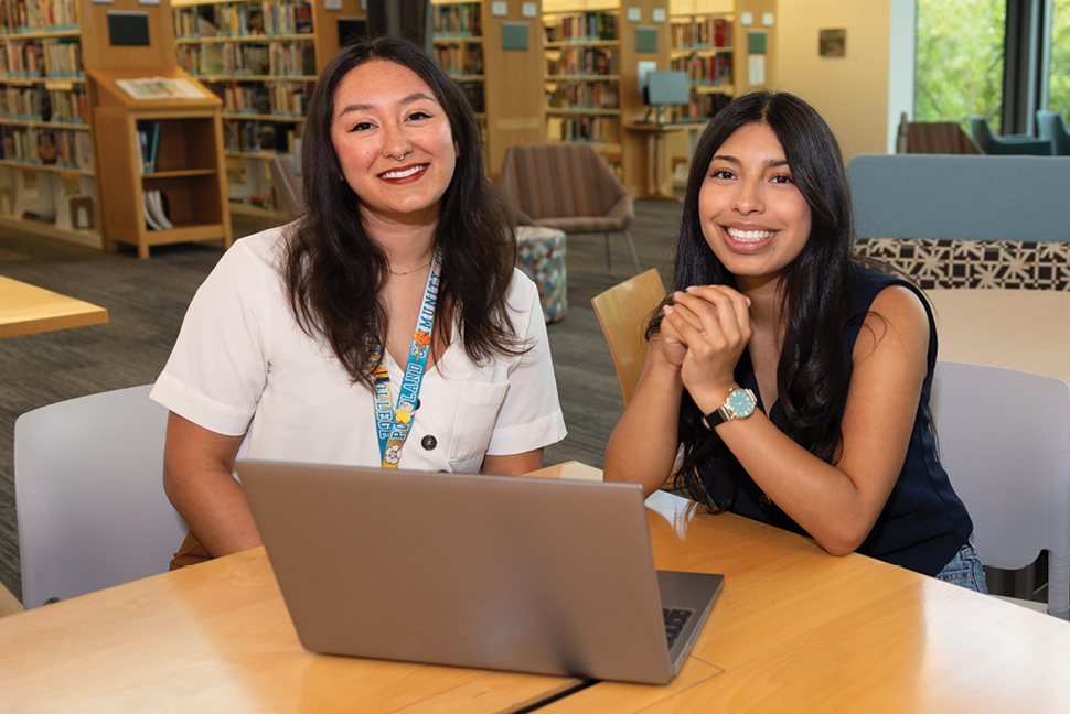 Two people sitting at table with laptop open and smiling directly at the camera.