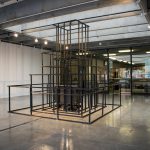 Large scale sculpture made of wood, in a pyramidal form, resembling a jungle jim play structure. Wood is painted black; in the center of framelike structure is a wooden box.