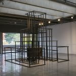 Large scale sculpture made of wood, in a pyramidal form, resembling a jungle jim play structure. Wood is painted black; in the center of framelike structure is a wooden box.