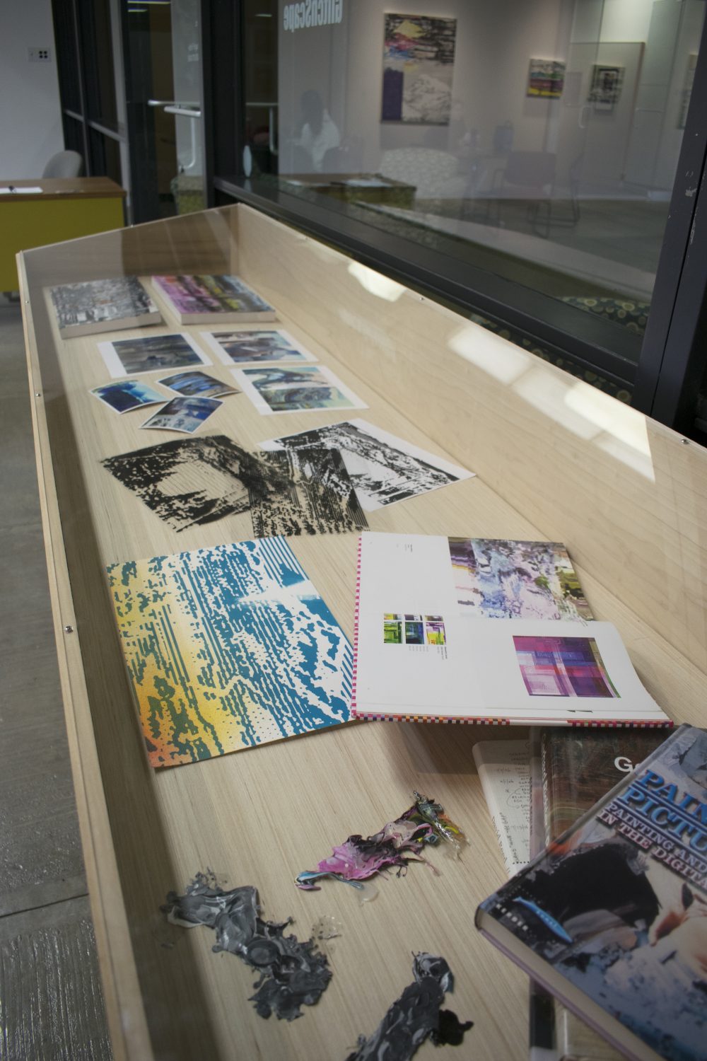 View of case that contains materials used to the paintings in the exhibition: prints, transparencies, paint, books.