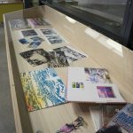 View of case that contains materials used to the paintings in the exhibition: prints, transparencies, paint, books.