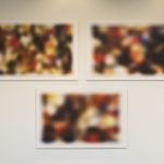 3 abstract, multicolored rectangular photos, hung on a gallery wall, 2 on top and 1 below.