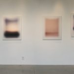 Wall of gallery with 10 photographs of simple abstract landscapes that are arranged in a wave pattern.