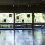 Panorama view of gallery with abstract photos on left and right sides, and in the middle the floor to ceiling windows with photos mounted on the glass and a view of trees outside.