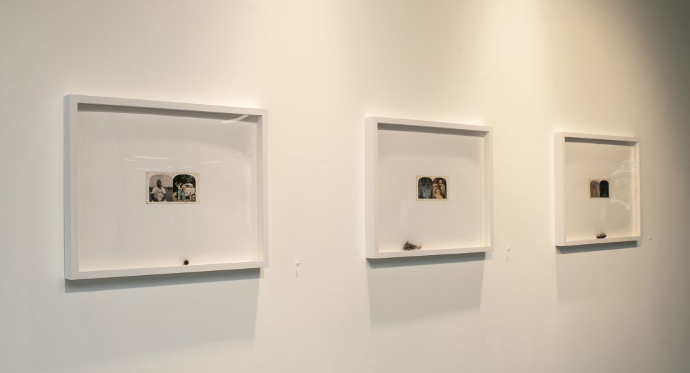 Three framed prints on wall; each has a small printed image of figures at the center, and a small lock of human hair at the bottom of the frame.