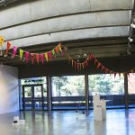 panorama of gallery with string of flags on ceiling, sculptures on floor, paintings and drawings on walls