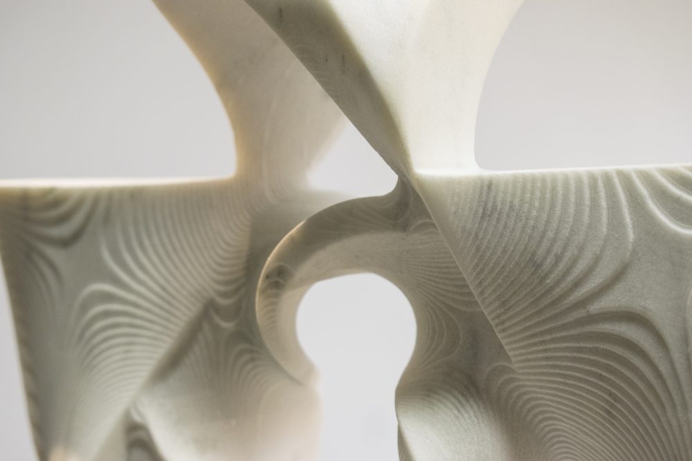 Close up view of marble sculpture in shape of a cross, showing carved wavy lines.