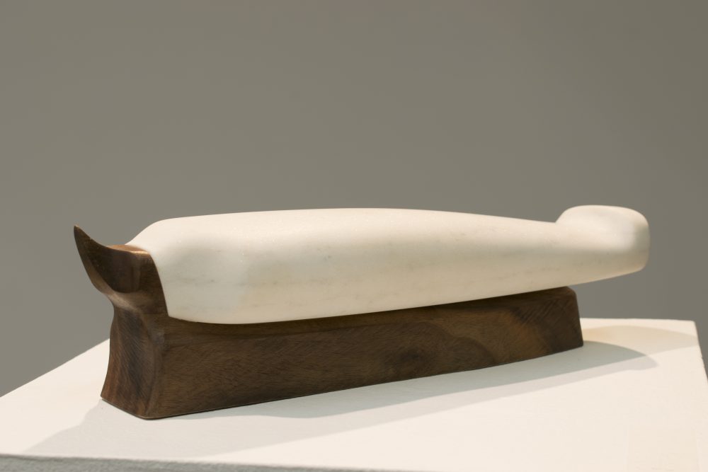 Small marble sculpture of abstract bird form, laying horizontally on dark walnut base.