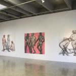 Four large scale drawings, each with three nude figures, drawn in charcoal and watercolor, hung on wall in gallery.