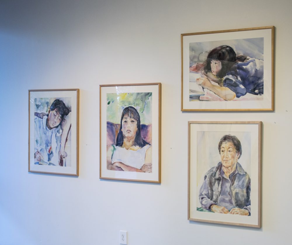 Four framed watercolors hang on gallery wall, each with a portrait of a member of the artist's family