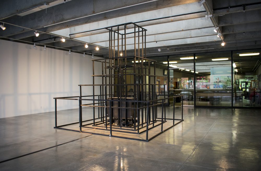 Large scale sculpture made of wood, in a pyramidal form, resembling a jungle jim play structure. Wood is painted black; in the center of framelike structure is a wooden box.