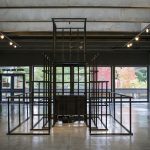 Large scale sculpture made of wood, in a pyramidal form, resembling a jungle jim play structure. Wood is painted black; in the center of framelike structure is a wooden box.