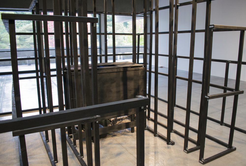 Detail view of wooden framed rectilinear sculpture, a black wooden box is in center.