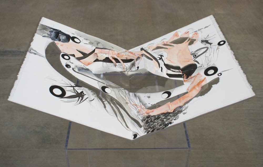 Paper pop-up book, folded open and seated on a plexiglass pedestal. The image in the book is an abstract painting with pale pink-orange arm and hand forms, and black and grey ink lines, circles and dots, all on a white background.