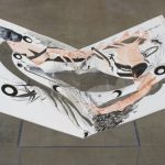 Paper pop-up book, folded open and seated on a plexiglass pedestal. The image in the book is an abstract painting with pale pink-orange arm and hand forms, and black and grey ink lines, circles and dots, all on a white background.