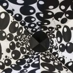 Detail view of folded paper drawing, showing a black circle at the center and lines of black circles with small white circles inside them radiate outward from the center.