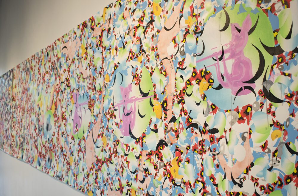 Side view of long, horizontal painting, with the closest part of the painting on the right side and the rest tapering off to the left. The images are abstract with an overall patterning of curved shapes in black, white, green, and blue and other colors.