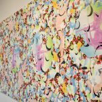 Side view of long, horizontal painting, with the closest part of the painting on the right side and the rest tapering off to the left. The images are abstract with an overall patterning of curved shapes in black, white, green, and blue and other colors.