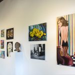 Installation view of gallery wall with multicolored and black and white paintings and drawings on a wall that recedes to the left. At the center of the wall is a ceramic sculpture of a male head.