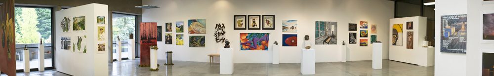 Panorama installation view of art gallery with many artworks on the far wall in the background, on additional walls to the left and rights, and of several pedestals in the middle.