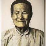 A painting of an older Asian woman in traditional clothing, with her hair pulled away from her face. The portrait is in sepia tones, highly photorealistic, and depicts just her head and shoulders, with her face looking directly at the viewer.