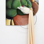 Large mixed media sculpture mounted on the wall with an element extending to the floor. A wood panel is painted in trompe l'oeil style with abstract curved forms. Colors include greens, greys, yellows, reds and white. A metal wire is attached at the bottom and curves up towards the middle of he panel. A long peach colored fabric is draped from the wire and falls to the grey floor.