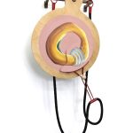 Large mixed media sculpture installed on a white gallery wall. A brown metal bar with three hooks is mounted to the wall on both ends, jutting out about 5 inches. A paddle shaped wood panel hangs from the center hook, and on it is a painting of a round yellow form on a pink circular background. A black rope with a red metal ring on each end hangs on the two other hooks.